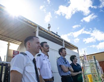 Student pilots andn instructor standing on tarmac watching plane fly by