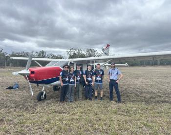 Pilot and passengers standing in front of plane on grass airstrip
