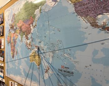 Large world map with strings and pins marking locations.